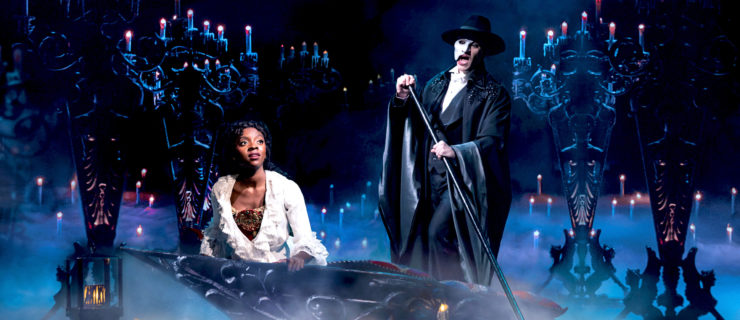 female wearing white sitting in a boat, male standing above wearing a cape and mask