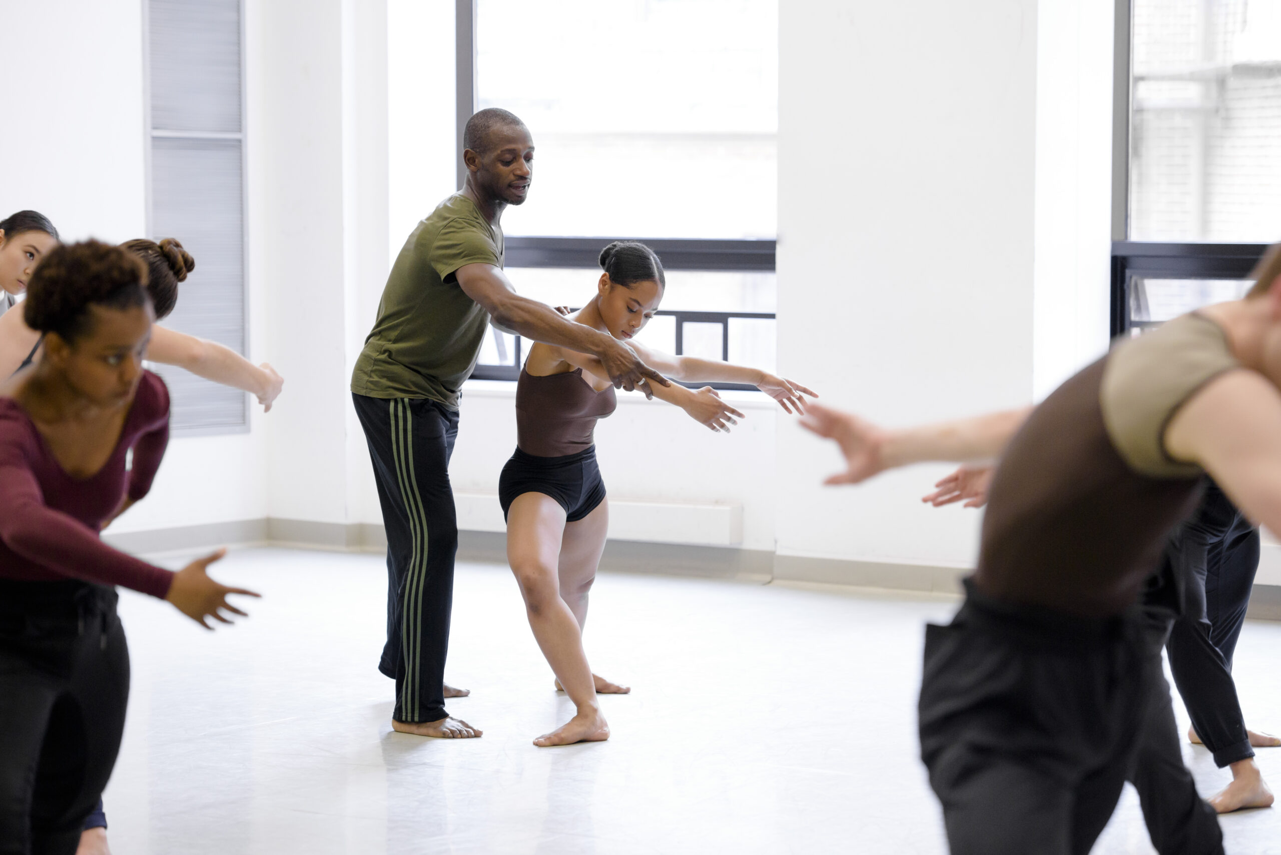 a male instructor guiding a female dancer's arm while taking class in the studio