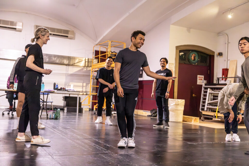 a blonde woman giving talking to dancers in rehearsal