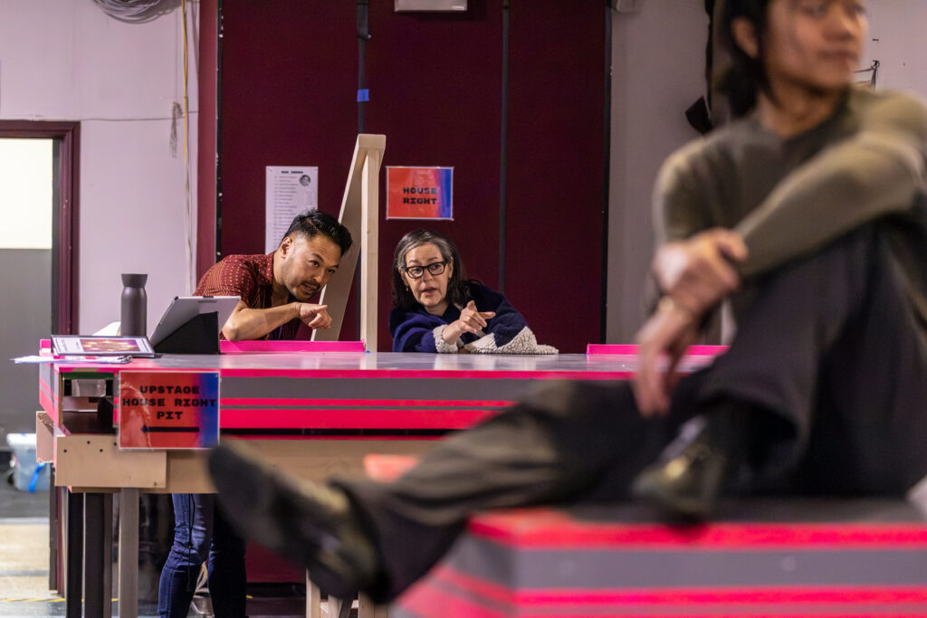 a woman and man watching rehearsal behind a pink striped table