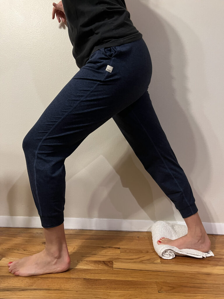 a dancer lunging back in a calf stretch with their back foot on a towel