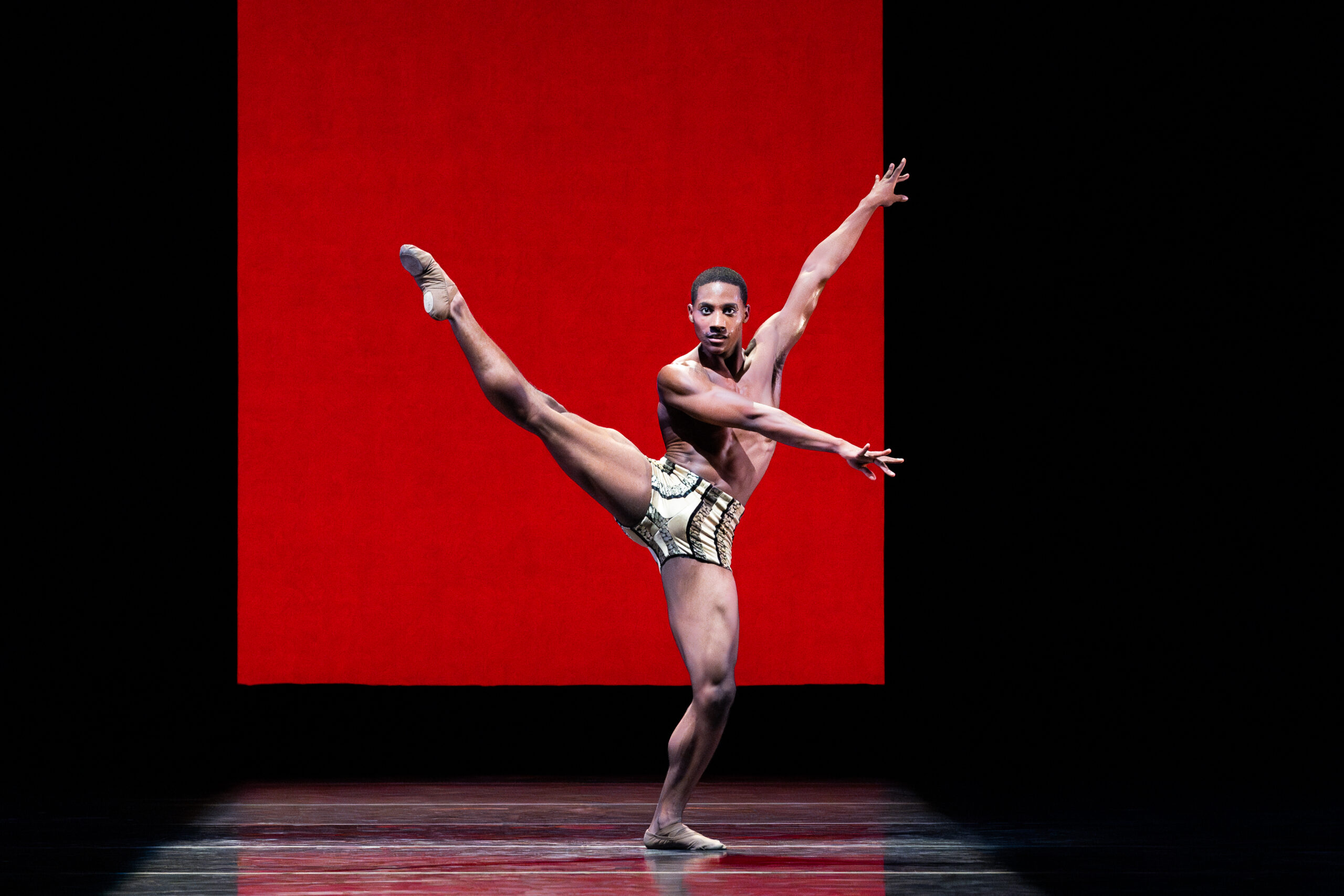 a male dancer wearing short extending his leg a la seconde with his arms going the opposite way