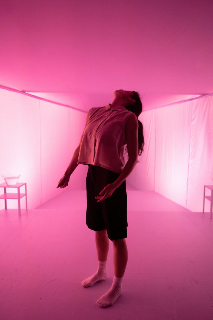 female dancer looking up in a pink lit room