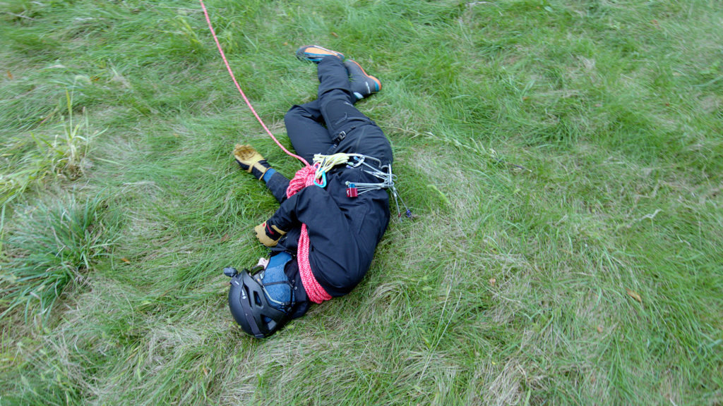 man laying on grass wearing helmet and rope harness