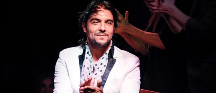 A man wearing a white jacket and polka dot scarf sitting in a chair clapping