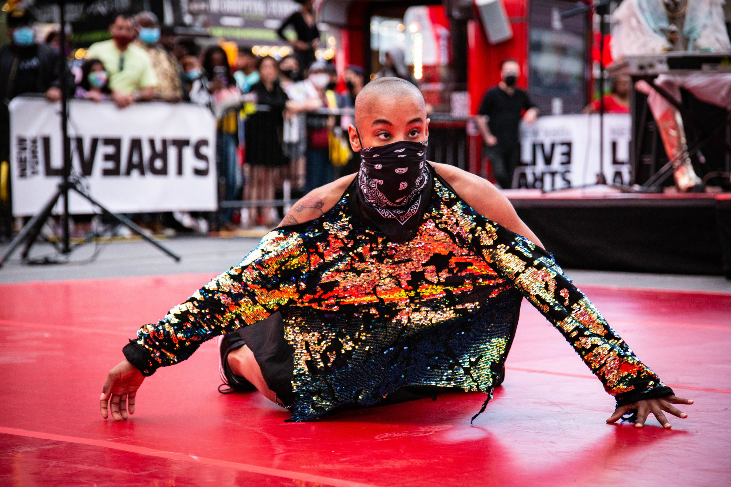 Jasmine Hearn crawls on a red stage, a mask over her mouth, audience behind her