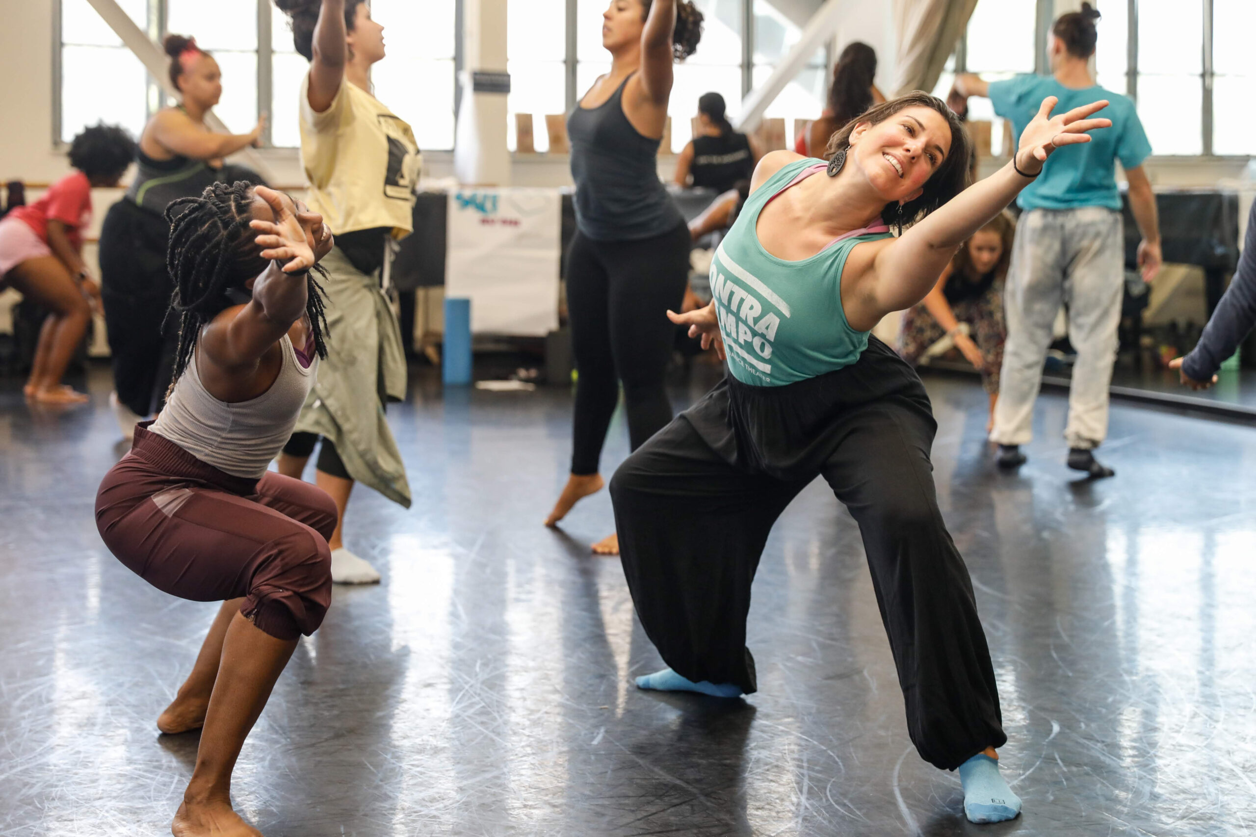 two female dancers mirroring each other while lunging side and reaching long with their arms
