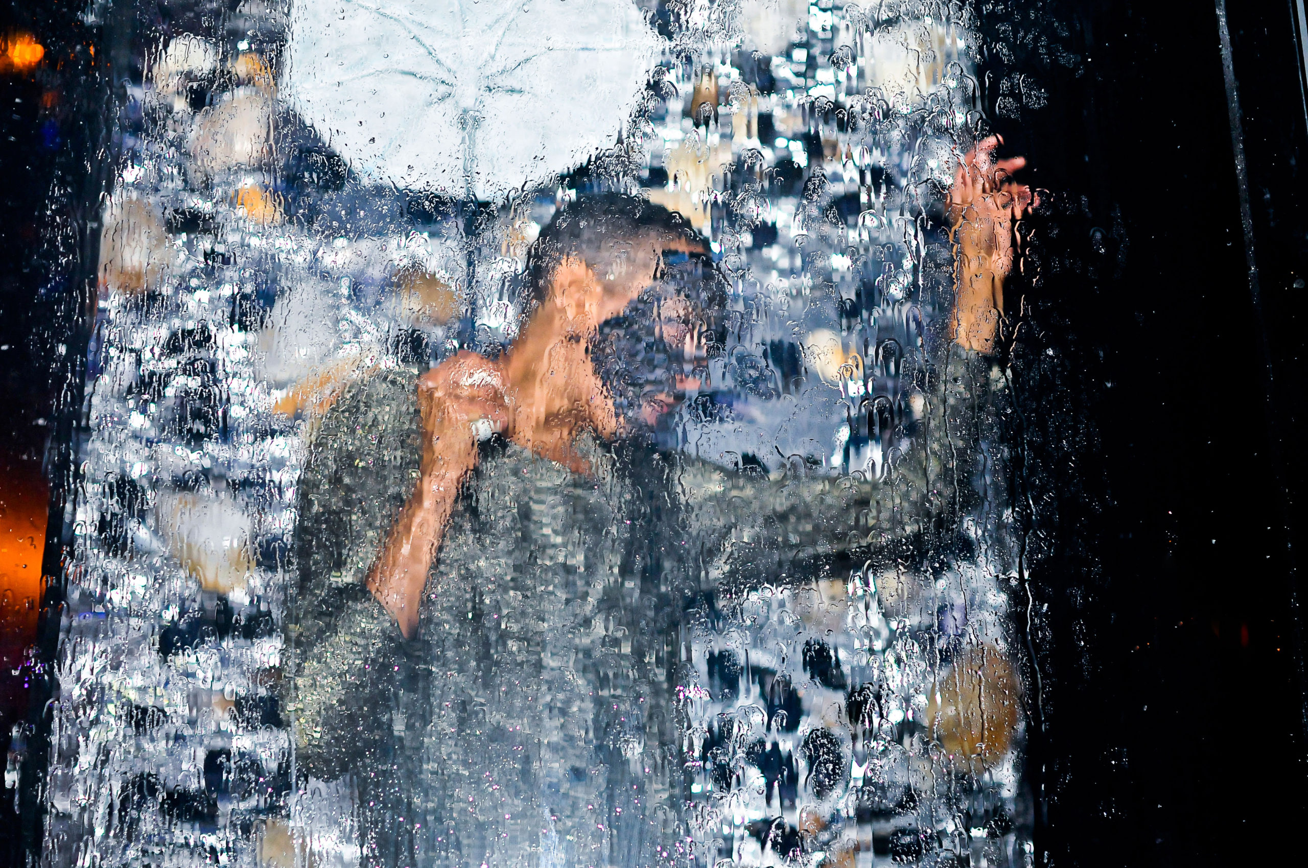 dancer under waterfall wearing grey shirt and mask, holding an umbrella