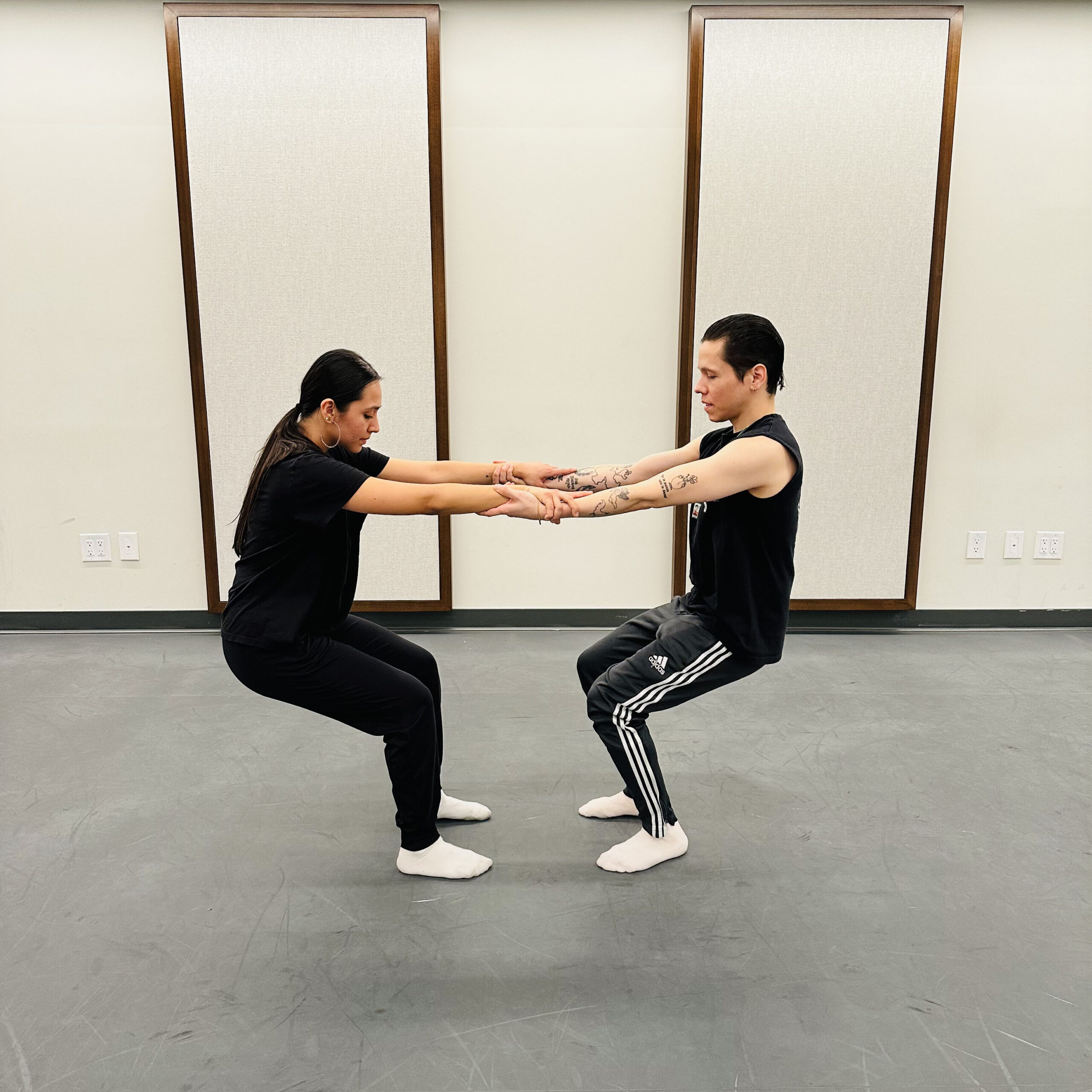 a male and woman facing each other while holding each other's forearms and bending their knees
