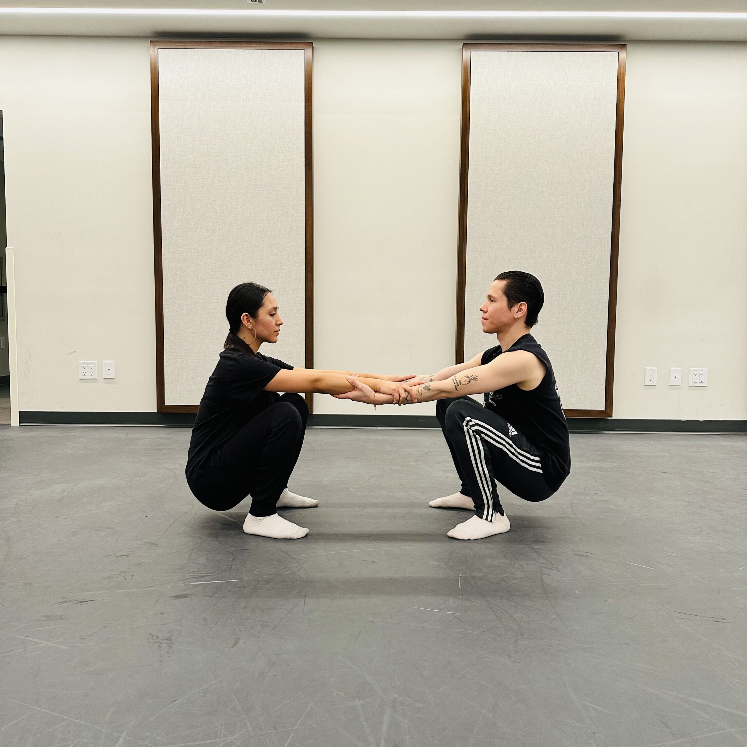a male and woman facing each other while holding each other's forearms and bending into a full squat