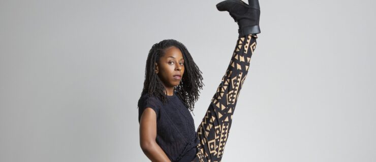 a female dancer wearing patterned pants and a blue top kicking her leg front